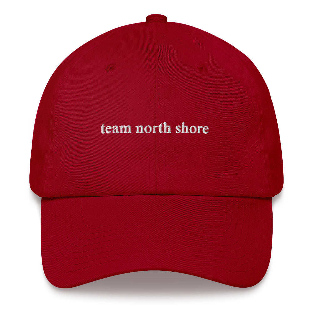 red baseball hat that says "team north shore" in white lettering