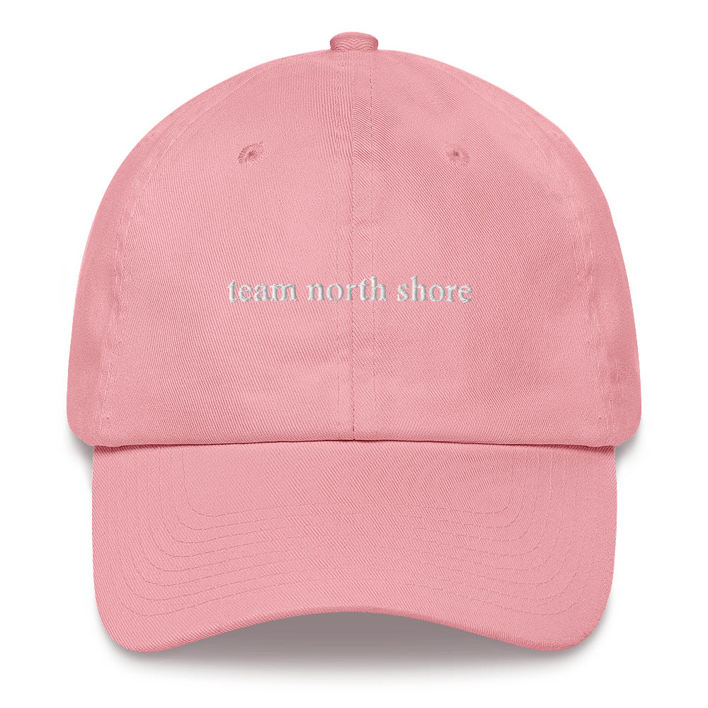 pink baseball hat that says "team north shore" in white lettering